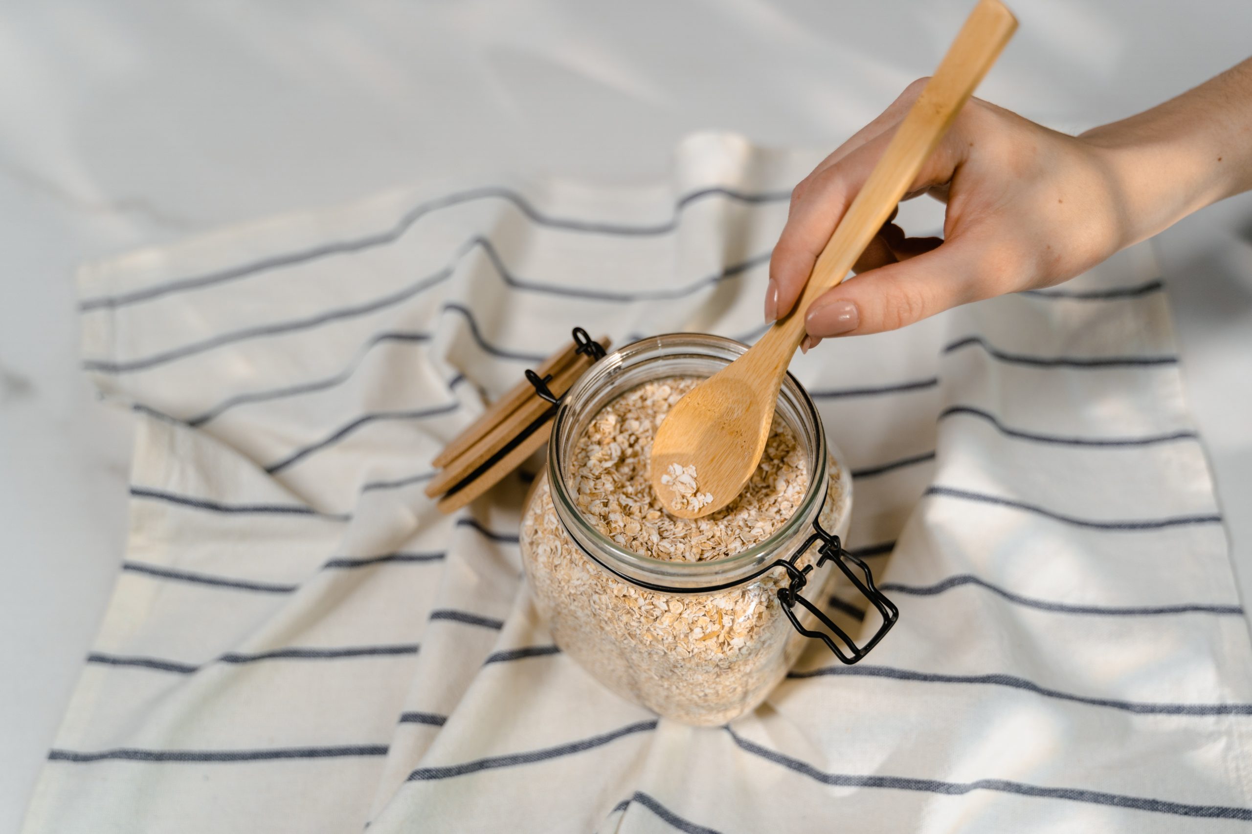 Wooden spoon in glass jar of oats on striped cloth.
