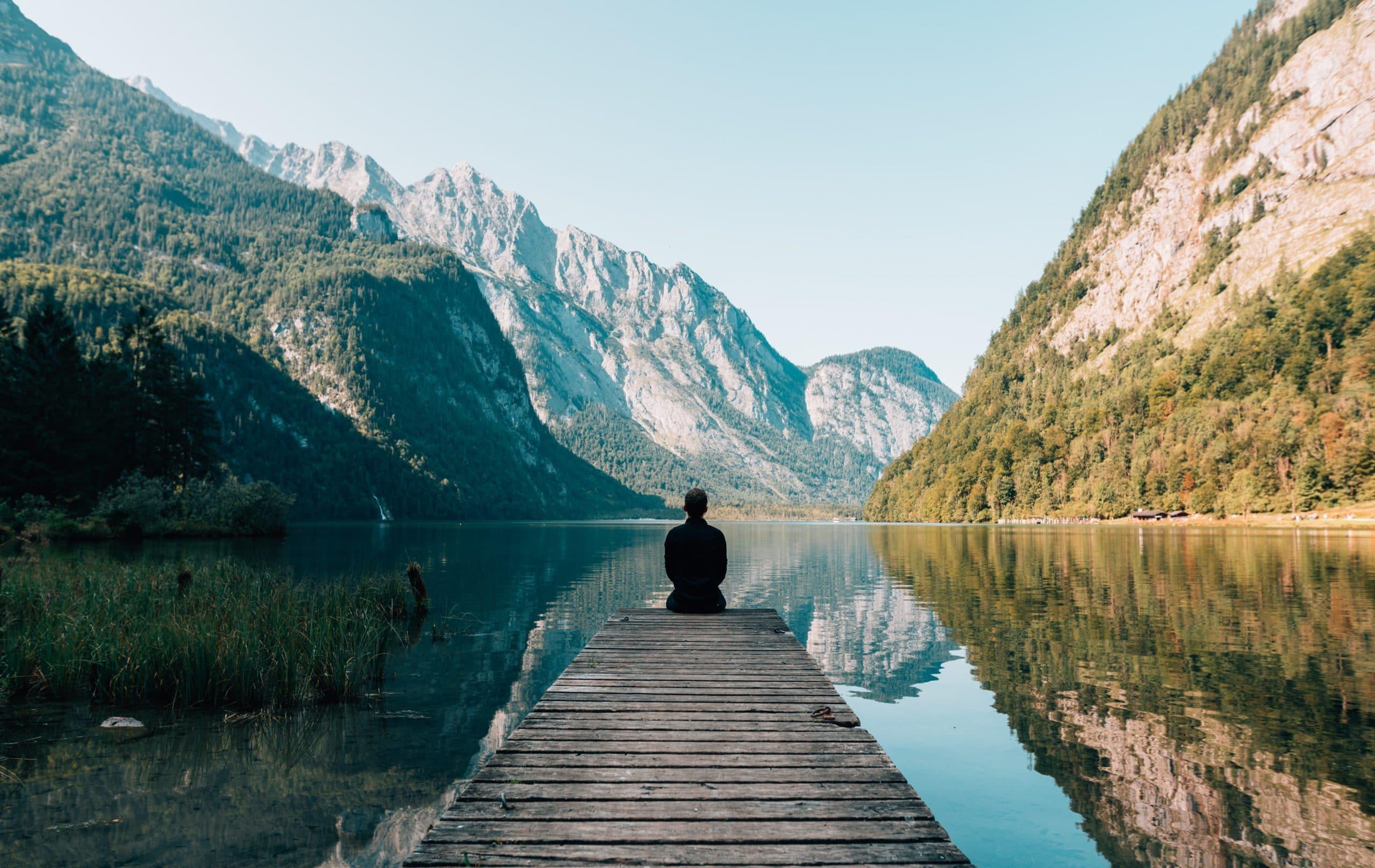 Man staring off into a lake with mountain reflection