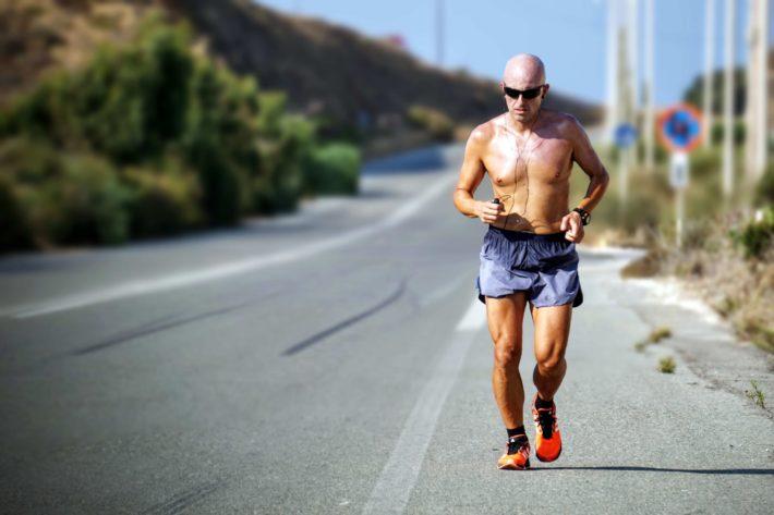 A shirtless, bald man running on a deserted road