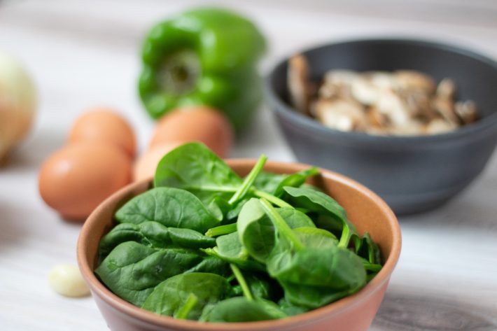 Spinach, eggs, and peppers in bowls, on a table